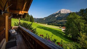 Un balcón de madera con un banco, con vistas a un campo verde y una montaña.