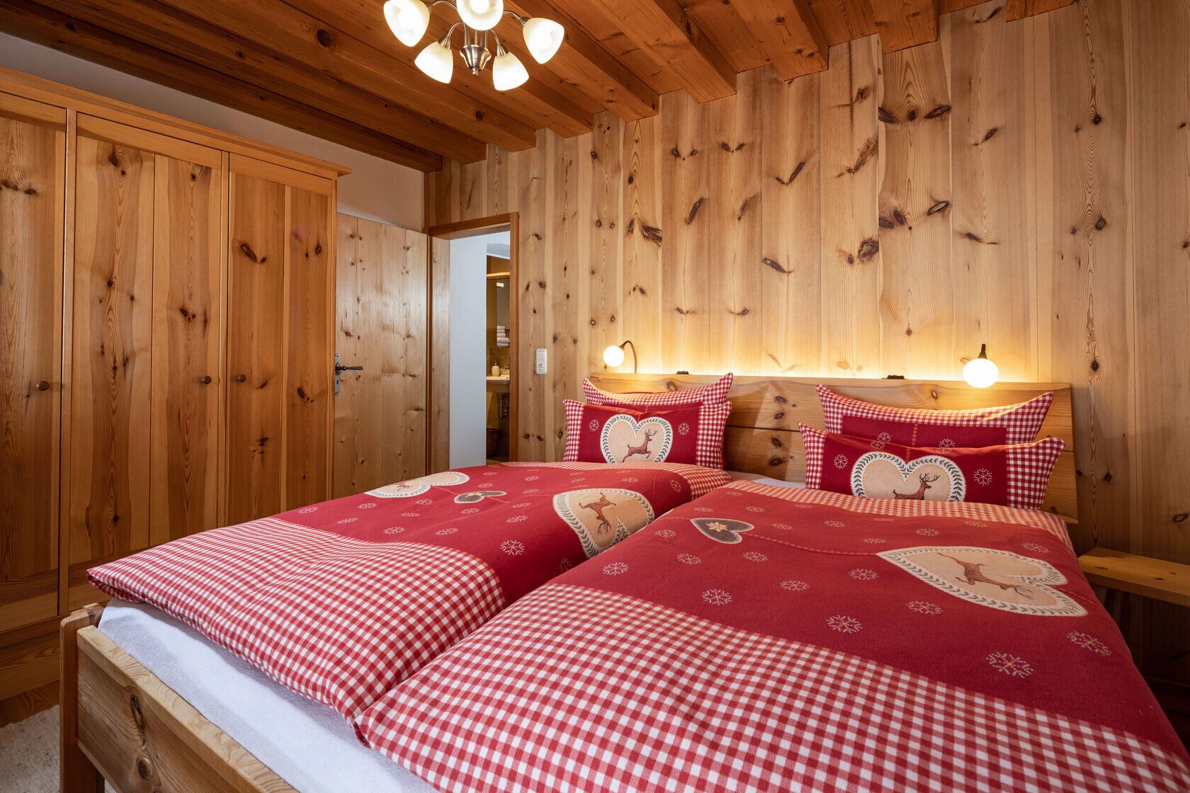 Un dormitorio acogedor con techo y paredes de madera, una cama con ropa de cama de cuadros rojos y blancos, y dos lámparas de noche.