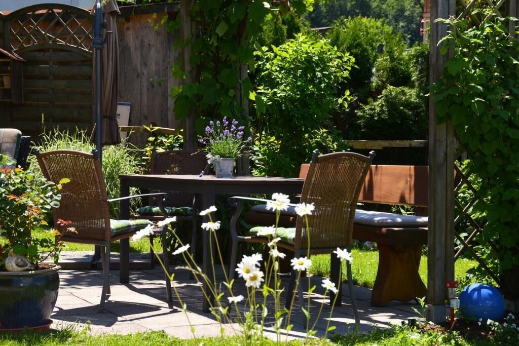 En udendørs terrasse med fletstole, et træbord og en bænk.