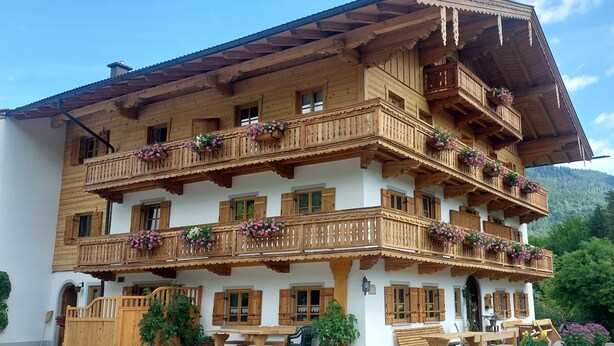 Un chalet traditionnel en bois, doté de plusieurs balcons, de meubles en bois et de plantes en pot.