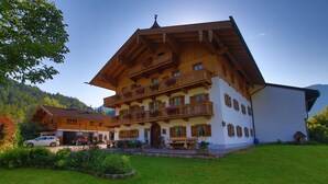 Un chalet traditionnel en bois, doté de plusieurs balcons, d’une terrasse couverte et d’une voiture garée devant.