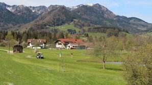 A golf course with a clubhouse, a small pond, and houses in the background with mountains. - I. Vacation apartment 72sqm, terrace, 1 bedroom, living room/bedroom, Loferer view (Ruhpolding)