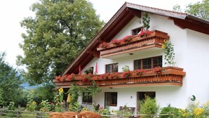 A two-story building with a balcony adorned with flowers and a wooden railing. - I. Vacation apartment 72sqm, terrace, 1 bedroom, living room/bedroom, Loferer view (Ruhpolding)