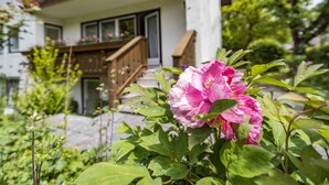 Una casa con escalera de madera que conduce a un balcón, rodeada de follaje y flores.