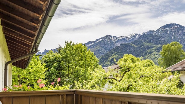 Una terraza de madera con una mesa blanca, rodeada de exuberante follaje y montañas al fondo.