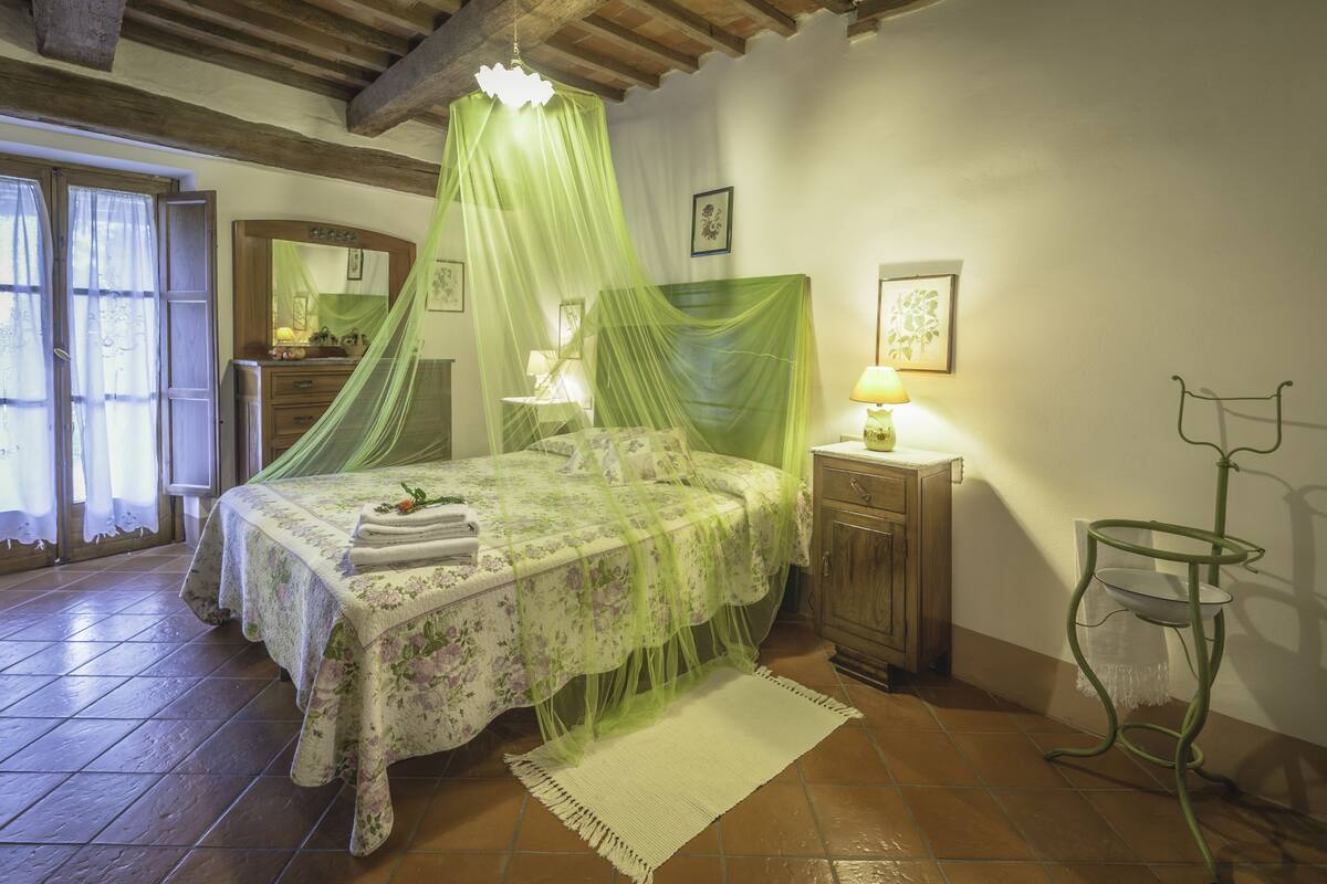 A bedroom with a bed, bedside table, lamp, and a hanging chair.