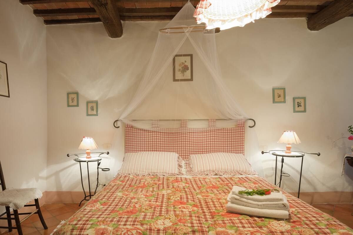 A bedroom with a bed, two bedside tables, a chair, and a hanging light fixture.