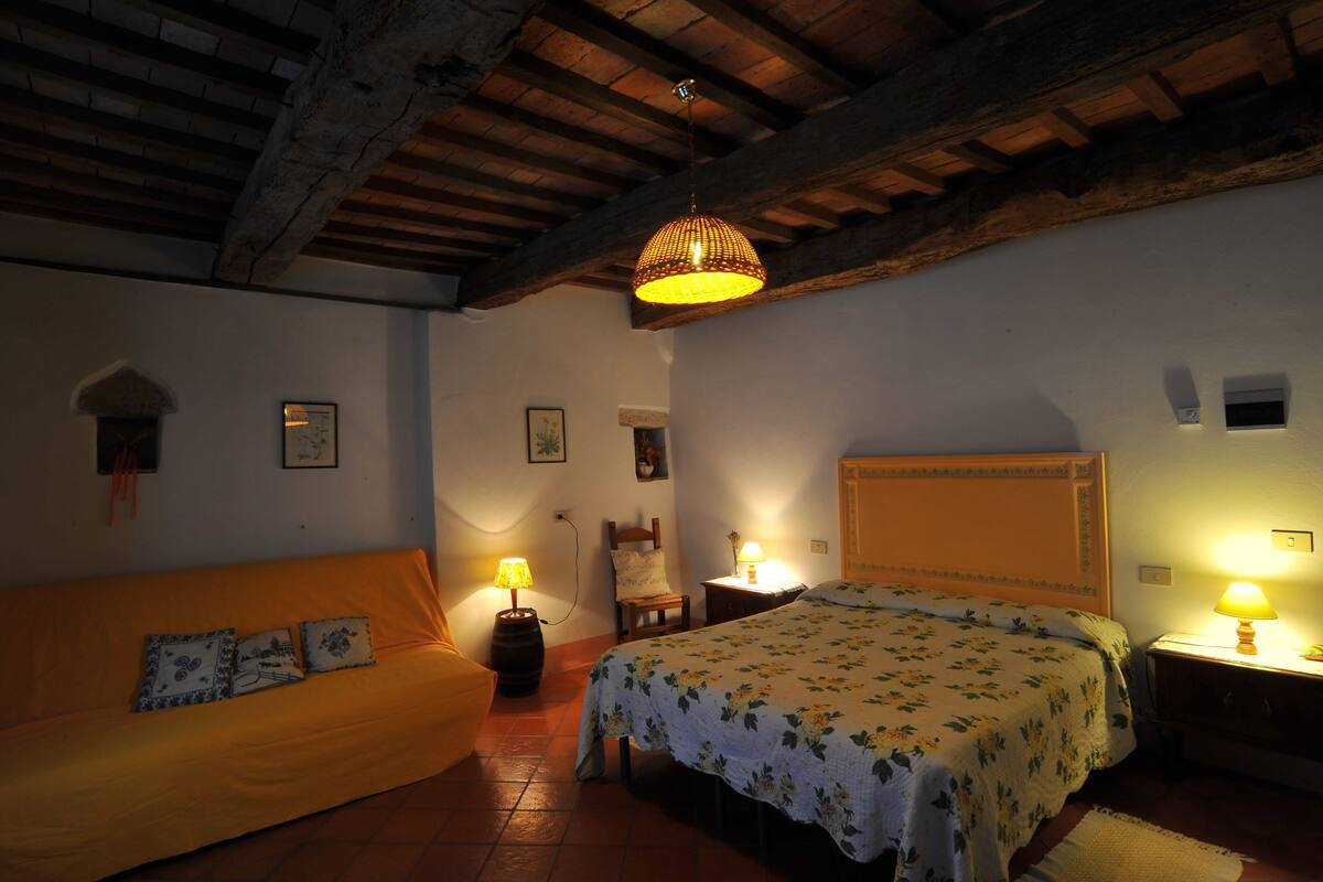A cozy room with a bed, a sofa, and a wooden ceiling.