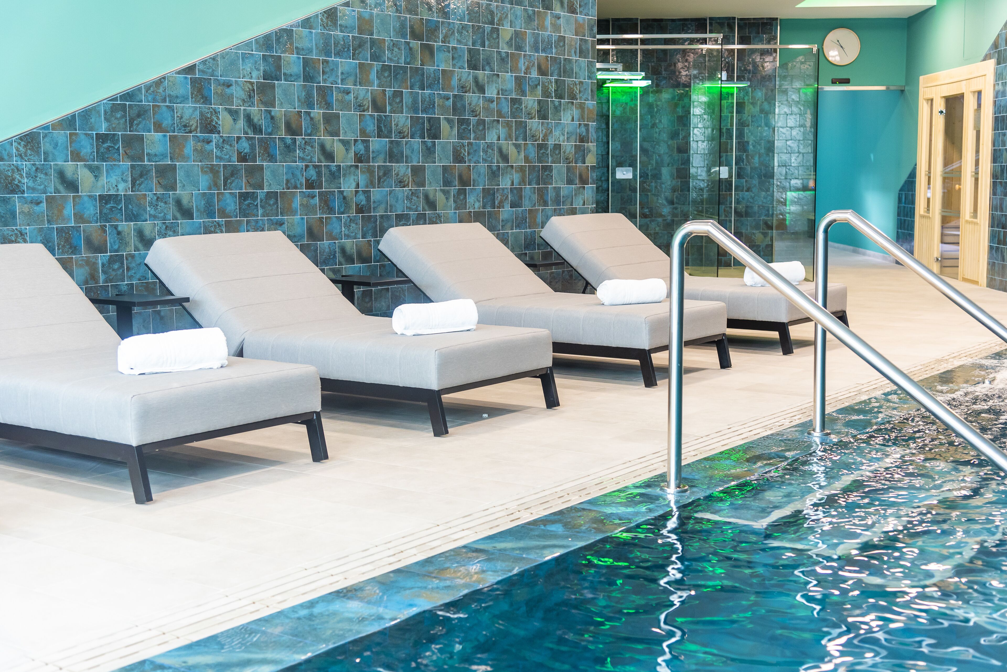 Zona de piscina con sillas de descanso y ducha envuelta en cristal.