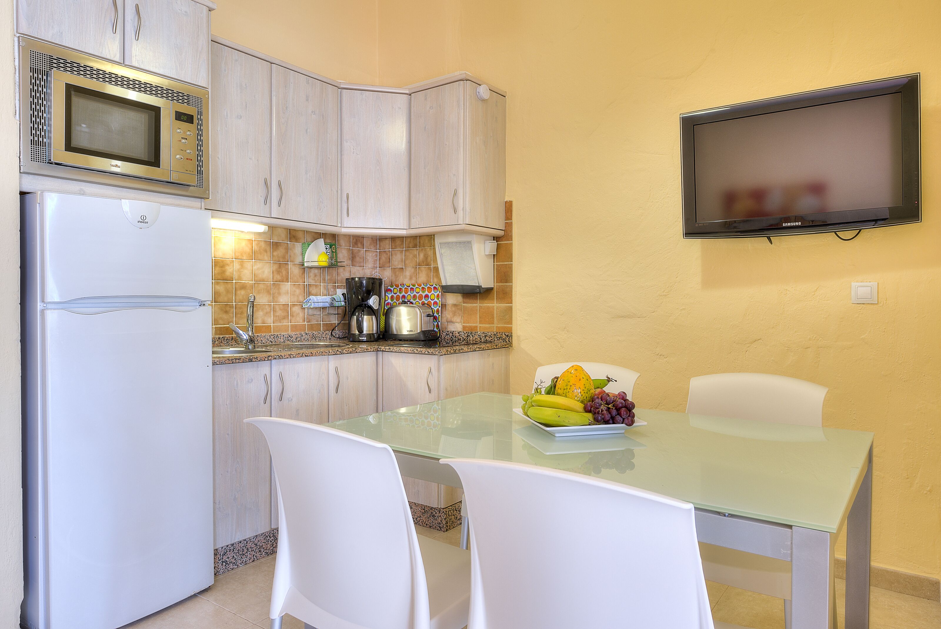 A compact kitchen with a microwave, refrigerator, and a small dining area with a glass table and white chairs.