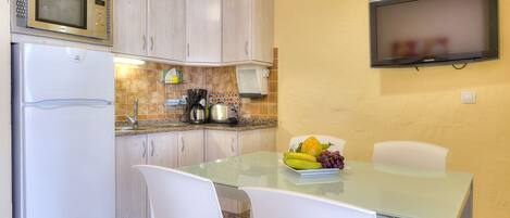 A compact kitchen with a microwave, refrigerator, and a small dining area with a glass table and white chairs.