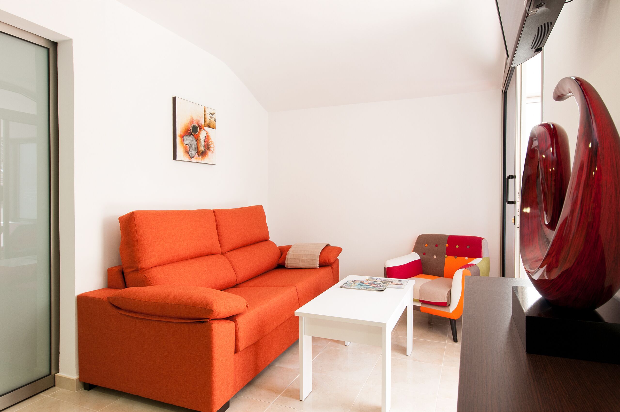 A modern living room with a bright orange sofa, a white coffee table, and a colorful chair.