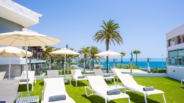 A rooftop lounge area with white lounge chairs and umbrellas, a pool, and a view of the ocean. - Casas Pepe Apartments & Spa- Adults Only (San Bartolomé de Tirajana)