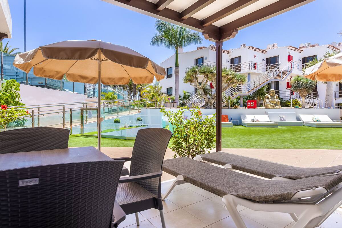 Ein Poolbereich mit Liegestühlen und Sonnenschirmen, mit freiem Blick auf den Pool, sowie ein Gebäude mit einer Treppe und Palmen.