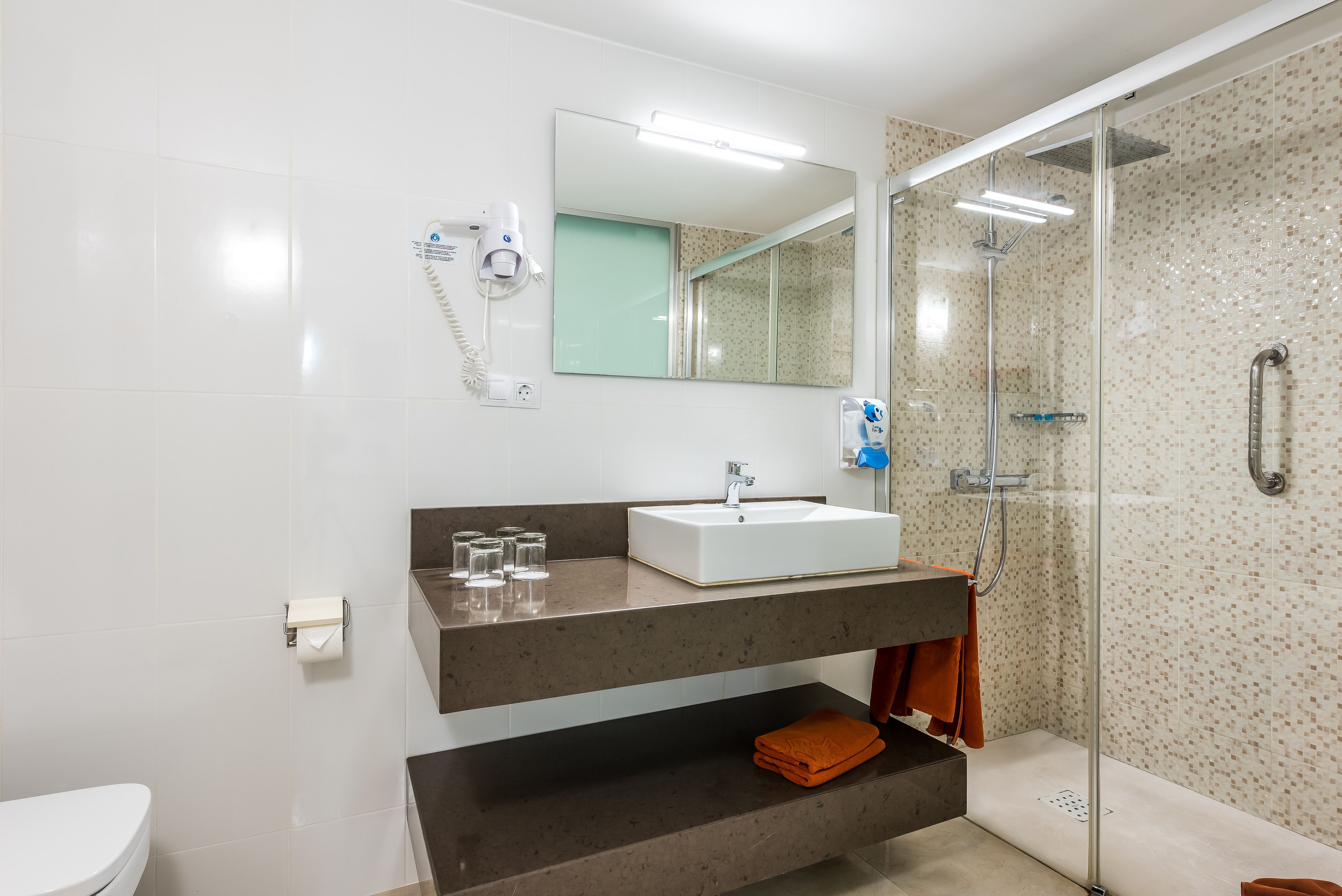 Un baño moderno con un lavamanos blanco, cabina de ducha con mampara de vidrio y un perchero para toallas.