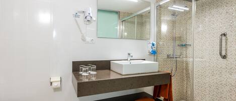Un baño moderno con un lavamanos blanco, cabina de ducha con mampara de vidrio y un perchero para toallas.