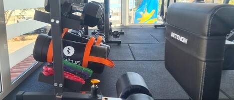 Ett gym med olika typer av träningsutrustning, inklusive en bänkpress, hantlar och en roddmaskin.