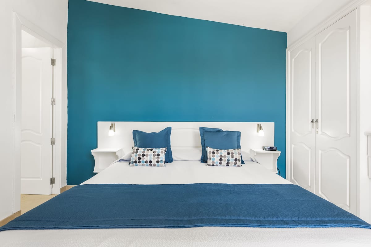 Ein Schlafzimmer mit einer türkisfarbenen Akzentwand, einem weißen Kopfteil und einer blauen Bettdecke.