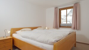 A single bed with a wooden frame, a bedside table with drawers, a lamp, and a window with curtains. - gemütliche Ferienwohnung für 1-4 Personen mit großem Balkon und Bergblick (Wohnung 2) (Bayerisch Gmain)