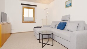 A modern living room with a grey sofa, a small glass table, a wooden cabinet, a television, a window with blinds, and a floor lamp. - gemütliche Ferienwohnung für 1-4 Personen mit großem Balkon und Bergblick (Wohnung 2) (Bayerisch Gmain)