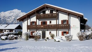 A two-story building with a balcony, surrounded by snow-covered bushes and a mountain in the background. - gemütliche Ferienwohnung für 1-4 Personen mit großem Balkon und Bergblick (Wohnung 2) (Bayerisch Gmain)