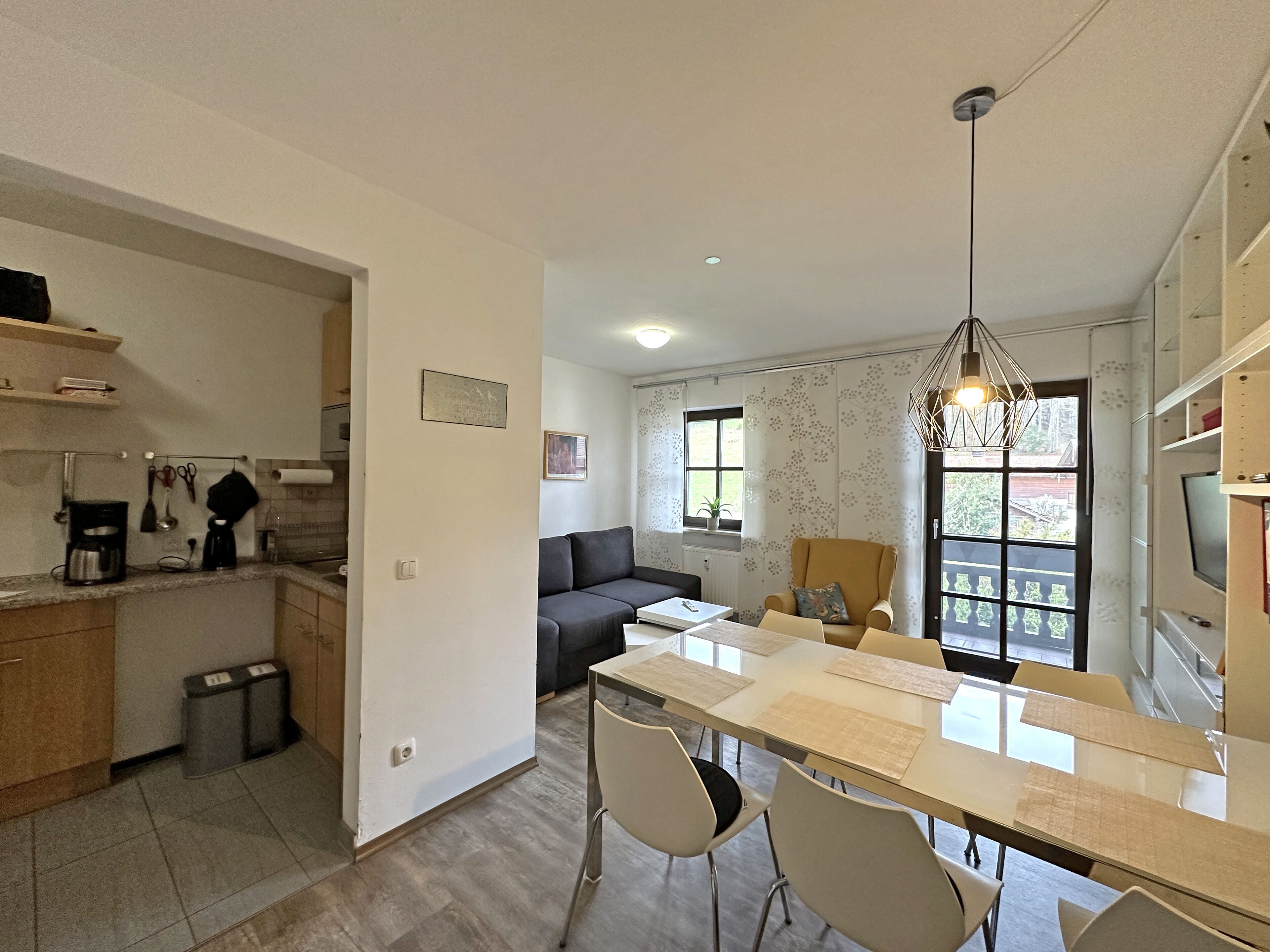 A modern kitchen with a dining area, a sofa, and a TV.