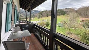 Un balcon avec une table et des chaises, donnant sur un paysage verdoyant parsemé de maisons et d’arbres.