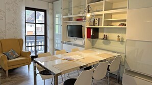 Un espace repas moderne avec une table en verre, des chaises blanches, un canapé et un téléviseur.