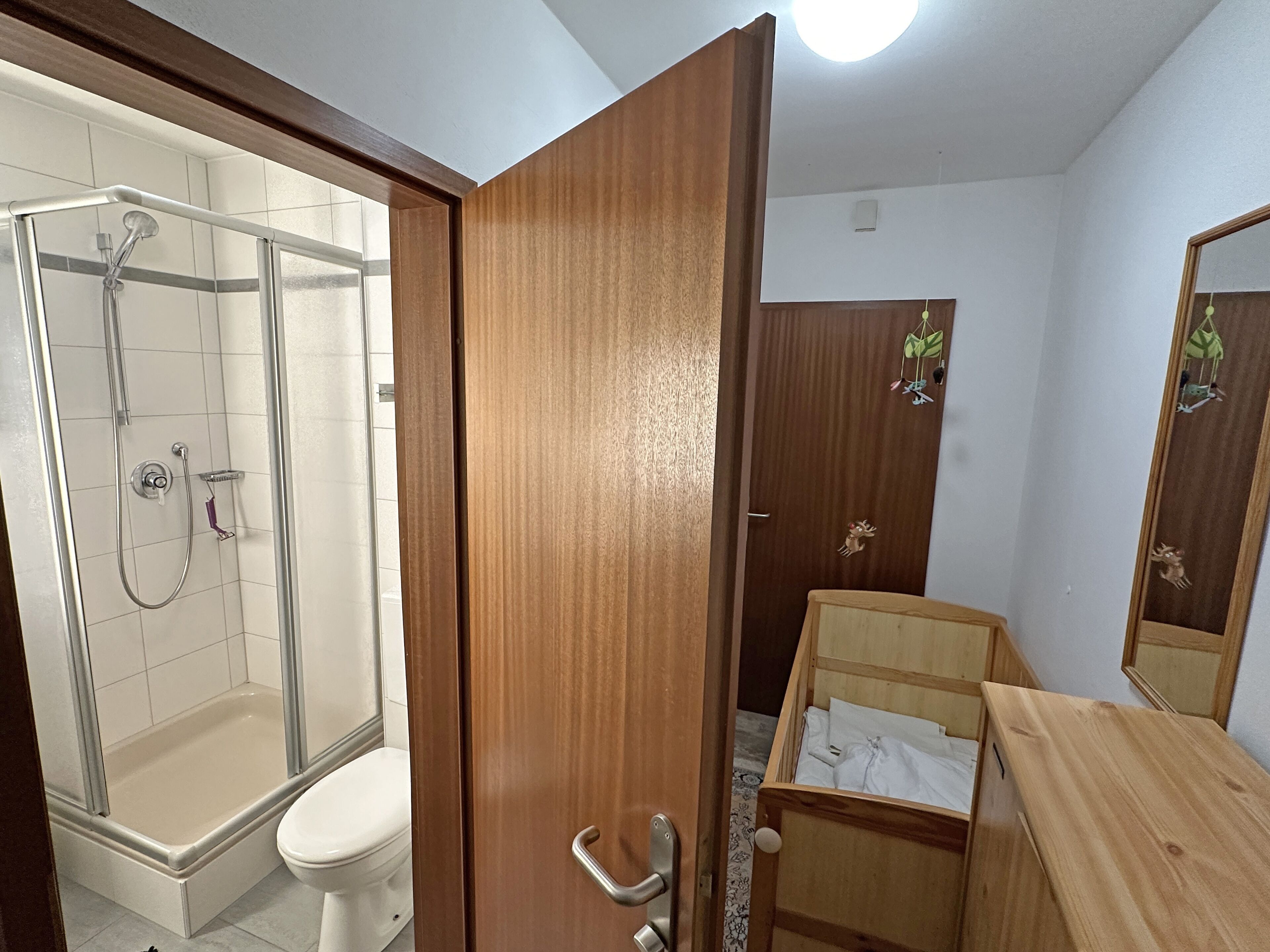 Une salle de bain avec une douche à parois de verre, une porte en bois, un meuble-lavabo en bois et un miroir.