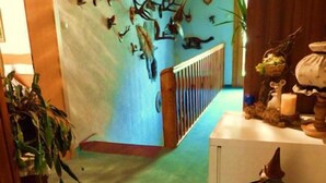 A hallway with a green carpet, a wooden railing, and a wall decorated with antlers. There are potted plants and a table with various items on it.