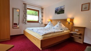 A wooden bed with a red polka dot carpet, a window with curtains, a mirror, a wall-mounted lamp, and a framed picture.