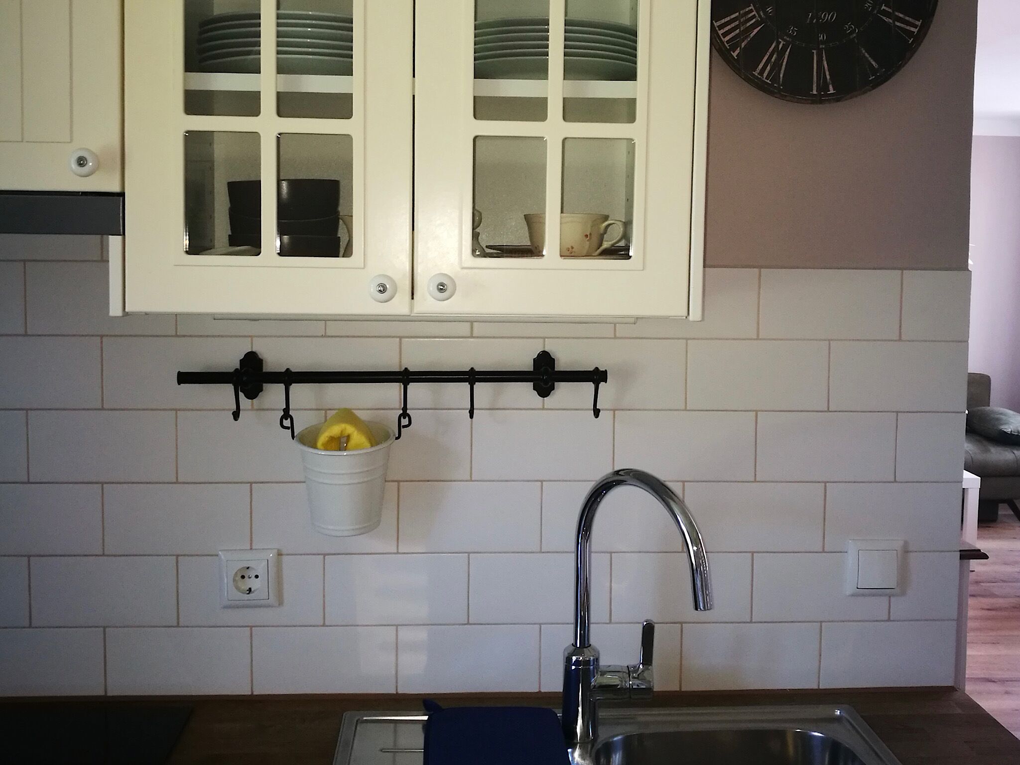 A kitchen with white cabinets, a hanging pot rack with a yellow fruit, a sink, and a clock on the wall.