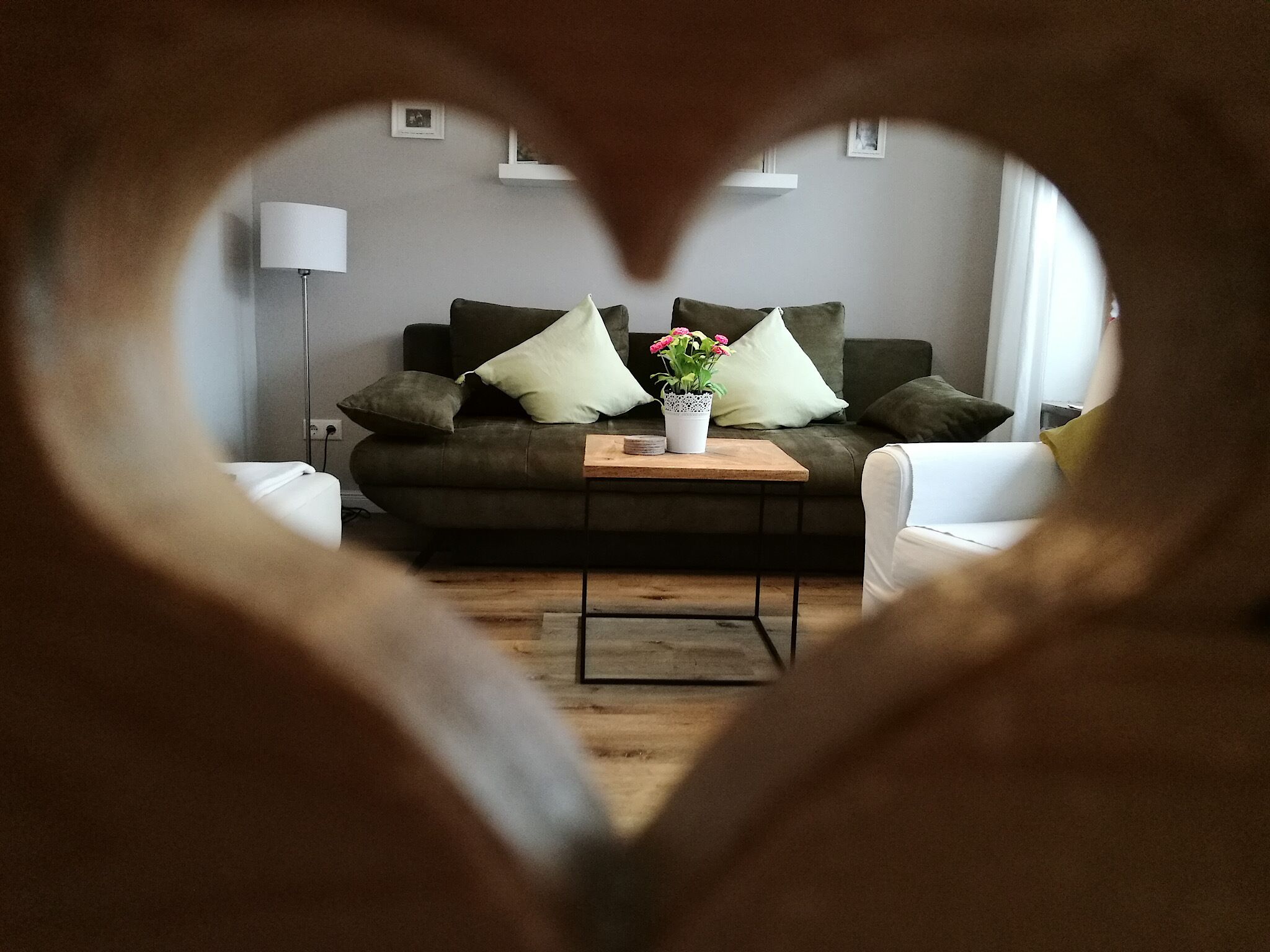 Ein Wohnzimmer mit einer Couch, zwei Kissen, einem kleinen Tisch mit einer Pflanze und einem weißen Sessel.