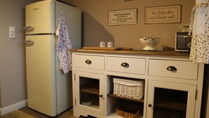 Une cuisine avec un réfrigérateur blanc d’époque, un plan de travail en bois et des meubles blancs dotés de tiroirs et d’étagères.
