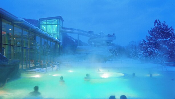 Un spa geotérmico con un edificio de cristal, una piscina de aguas termales y un tobogán de agua.