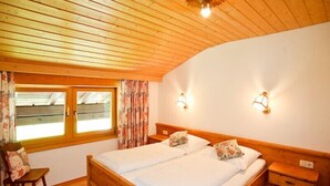 Dormitorio con paneles de madera, una cama doble, dos mesitas de noche, una silla y una ventana con cortinas.