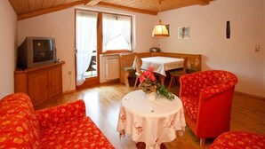 Una habitación acogedora con techo de madera, una mesa de comedor con sillas, un sofá y un televisor sobre un mueble.