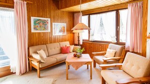 A cozy room with wooden walls, a sofa, two armchairs, a table with a plant, and a hanging lamp. - Apartment 2 upper floor 57sqm, balcony, kitchenette, 2 bedrooms, living room (Ruhpolding)