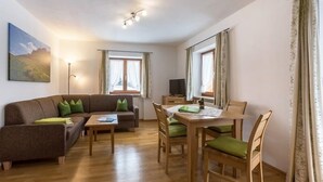 Un salon chaleureux avec un canapé marron, des coussins verts, une table à manger en bois avec des chaises et un tableau accroché au mur.
