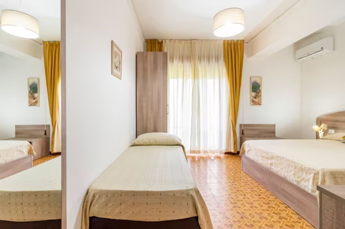 Camera d'albergo con due letti singoli, un ampio specchio, un armadio e una finestra con tende.