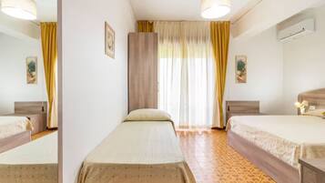 Camera d'albergo con due letti singoli, un ampio specchio, un armadio e una finestra con tende.