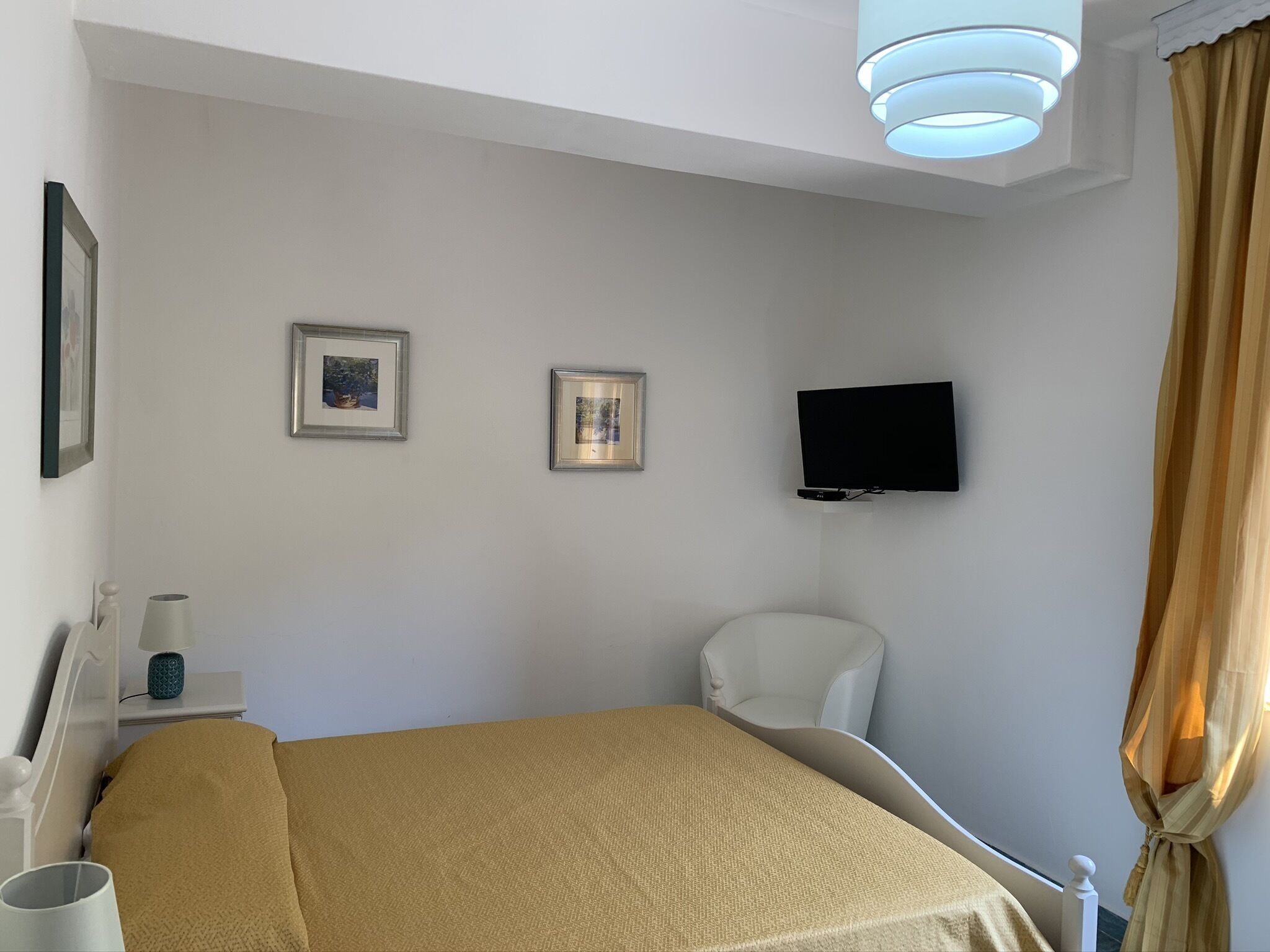 A hotel room with a bed, a television mounted on the wall, and two framed pictures.