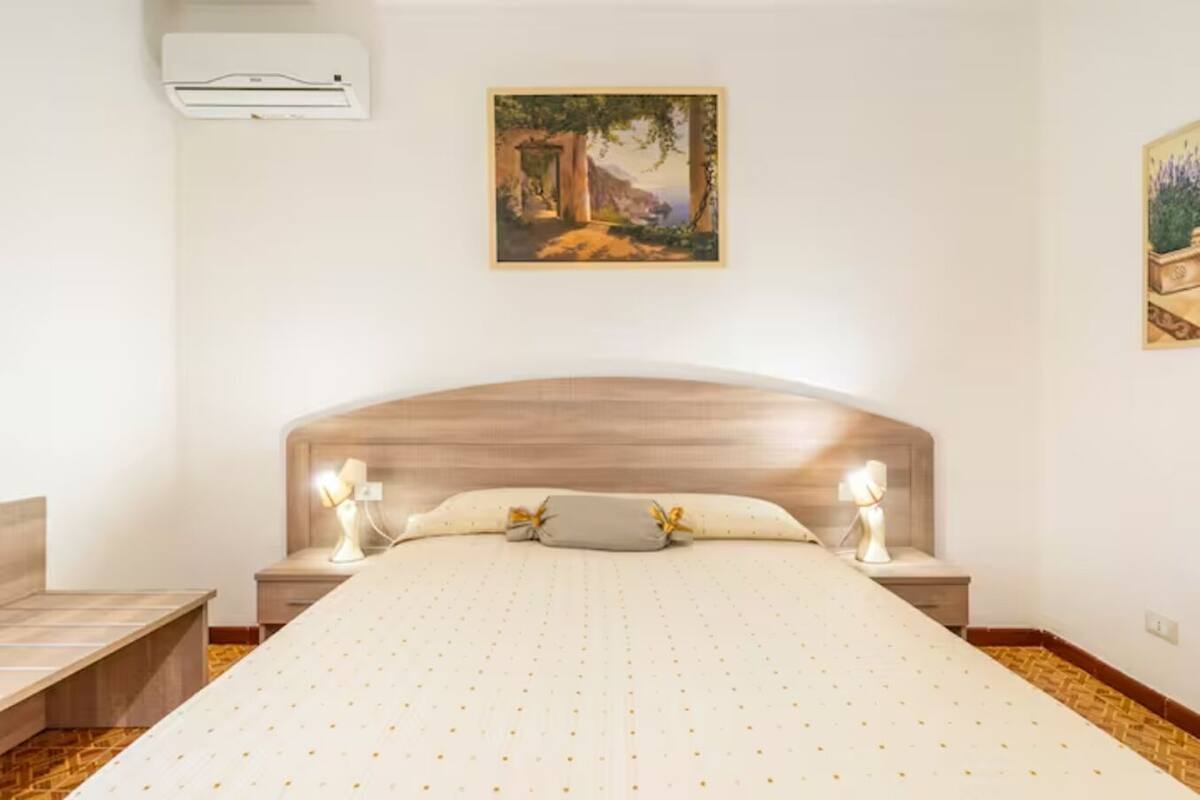 A bedroom with a large bed, two bedside tables, a nightstand, and a painting on the wall.
