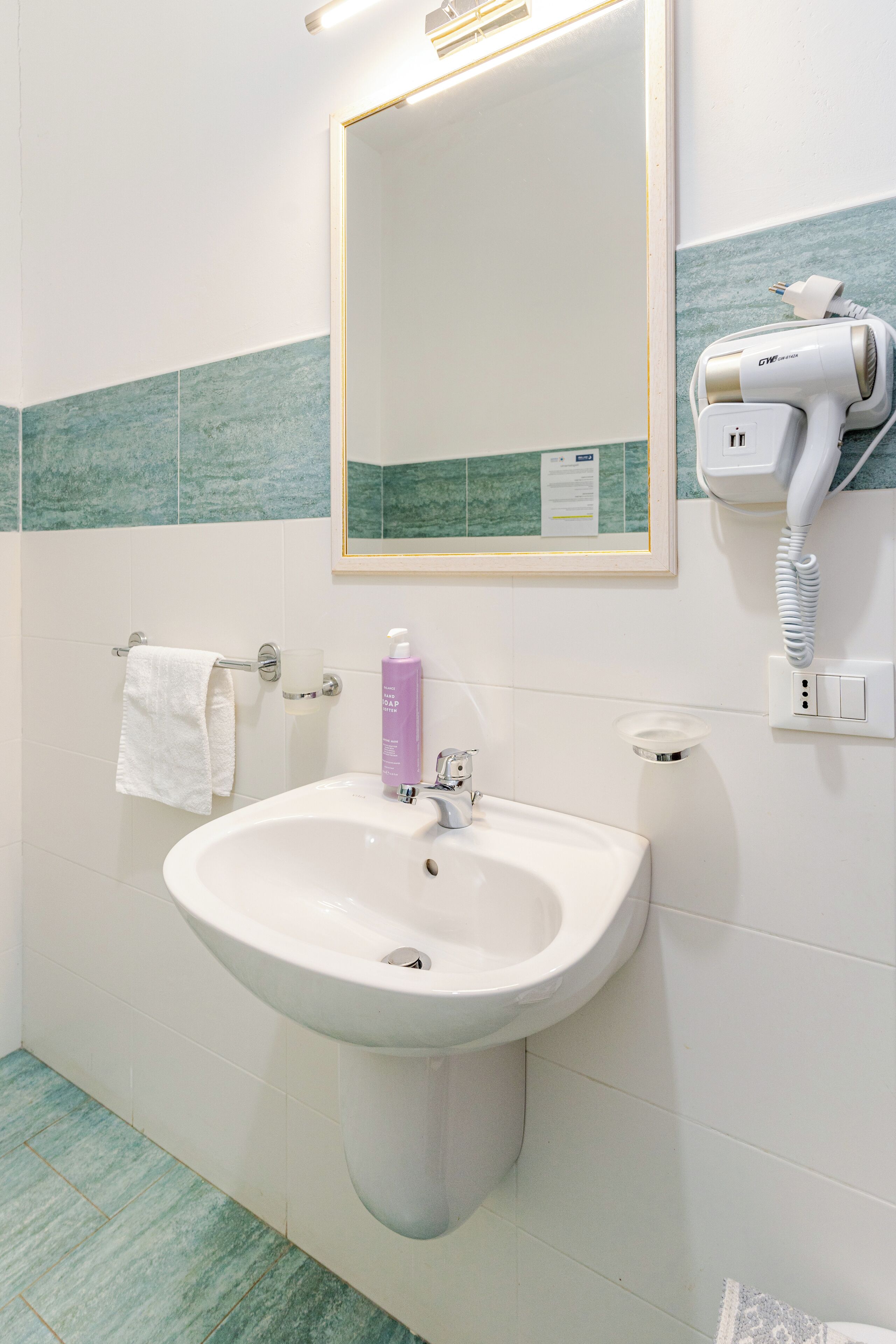 Een badkamer met een wastafel, spiegel, handdoekrek en een haardroger aan de muur.