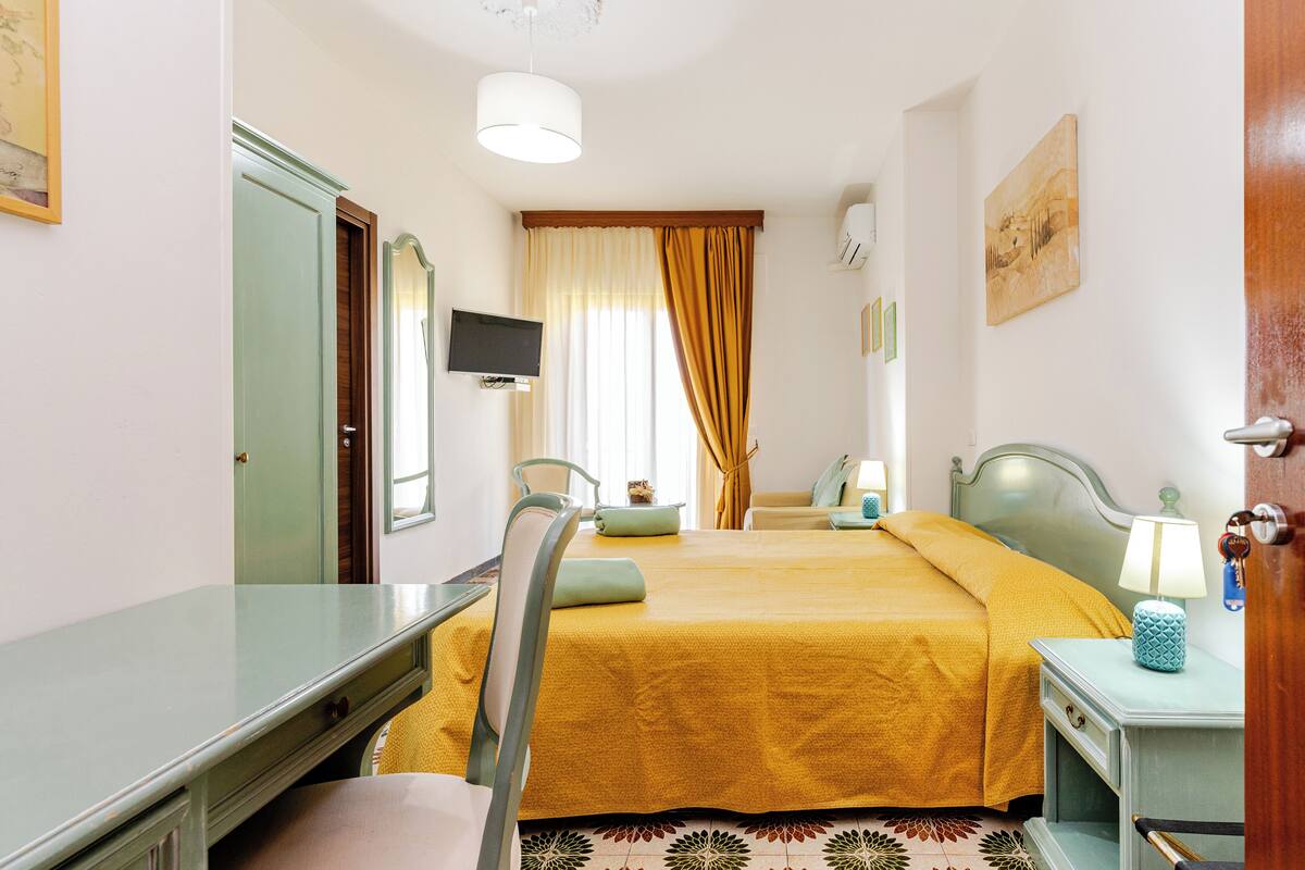 A hotel room with a bed, a desk, a chair, a television, and a window with curtains.