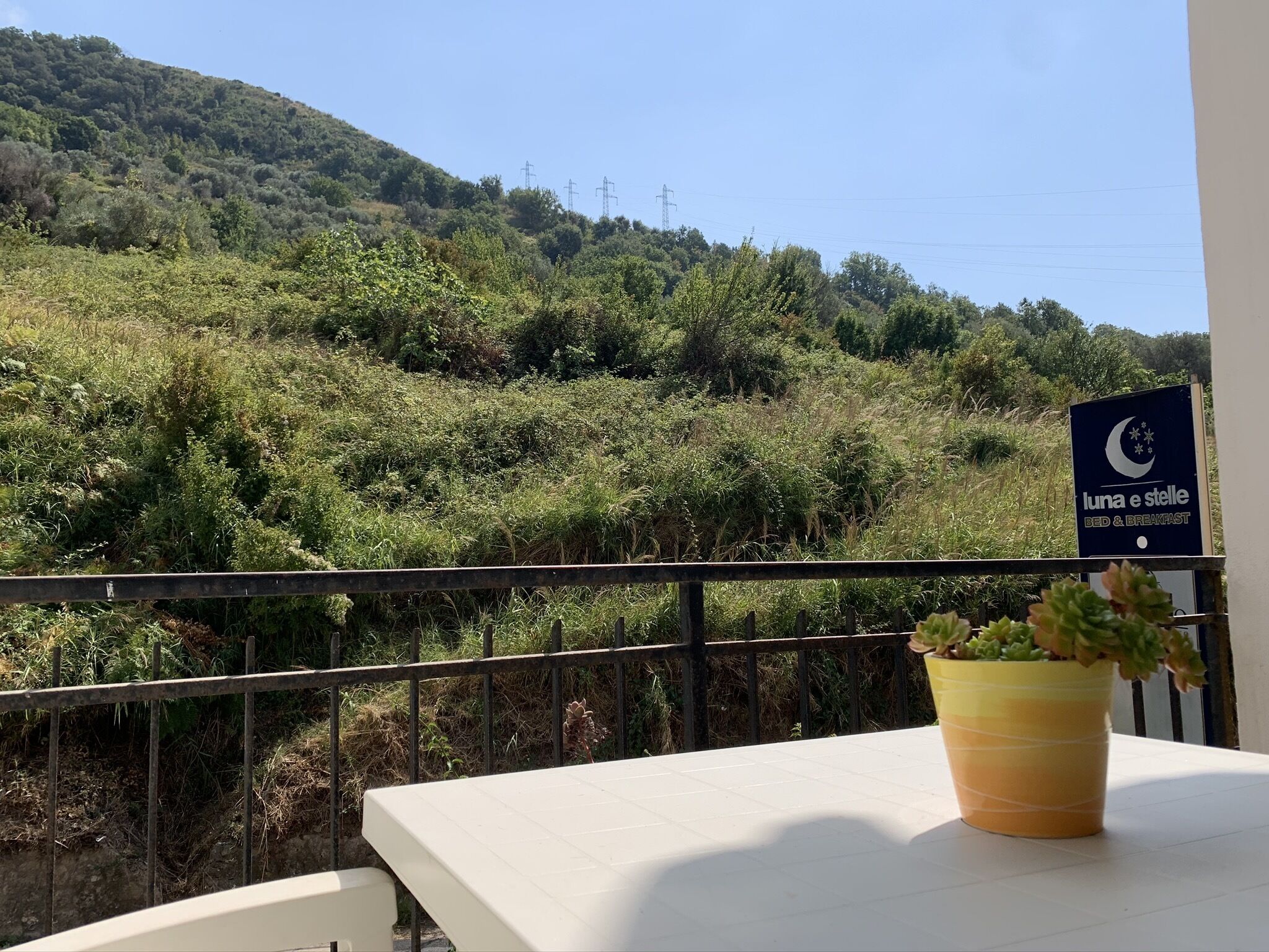 A balcony with a view of a lush green hillside and a sign for 'Luna e Stelle Bed & Breakfast'.