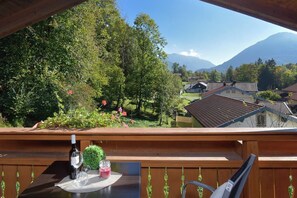 A wooden deck with a table set for two, overlooking a village and mountains.