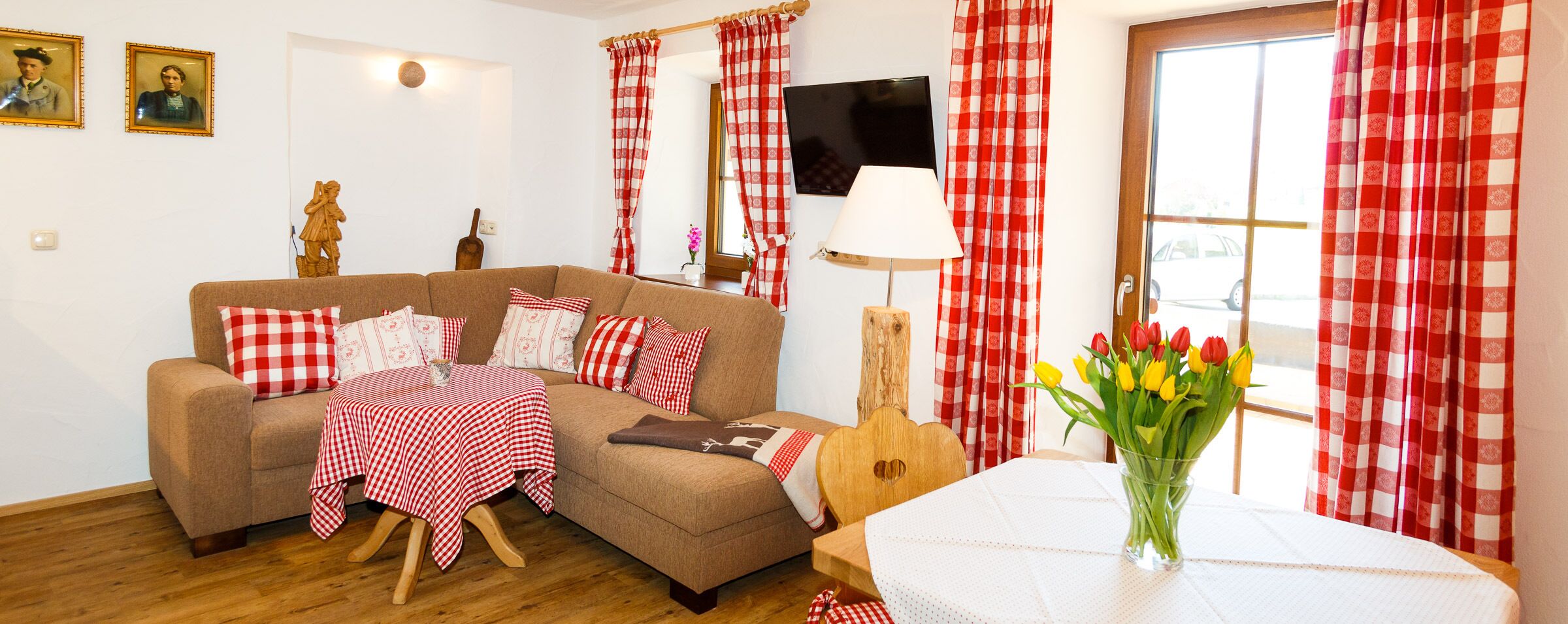A cozy living room with a sofa, a small table with a checkered tablecloth, a wooden guitar, and a vase of tulips.
