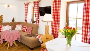 A cozy living room with a sofa, a small table with a checkered tablecloth, a wooden guitar, and a vase of tulips. - 8. vacation apartment Edelweiss, 45sqm, terrace, kitchen, 1 bedroom, 1 living room (Ruhpolding)
