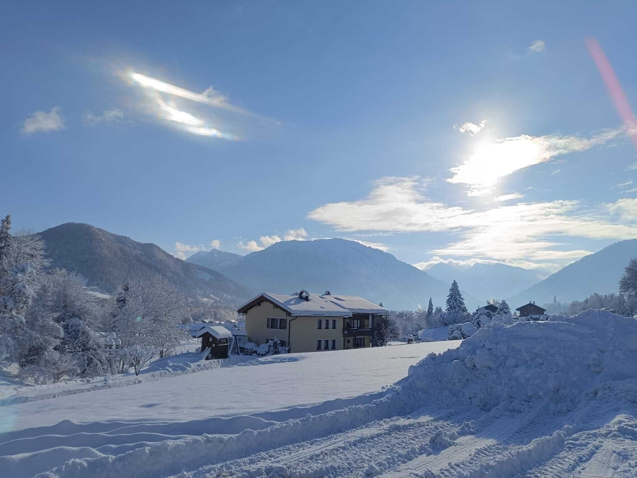A snow-covered landscape with a house and mountains in the background.